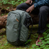 Elish sitting on a fallen tree in the woods with his the sage travel bag